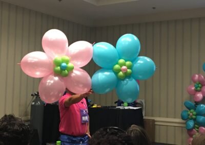 Balloon artist holding pink and blue flowers.