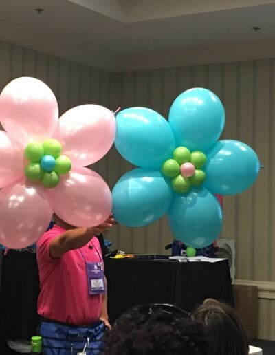 Balloon artist holding pink and blue flowers.