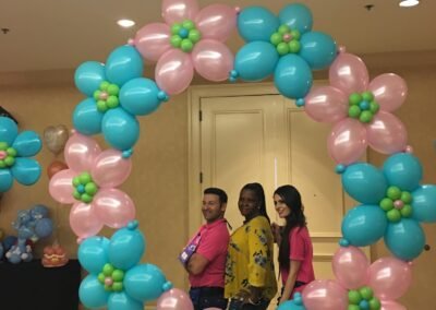 Three people posing with floral balloon arch.