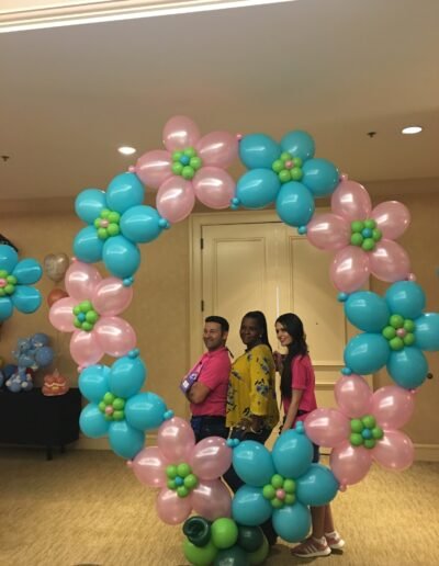 Three people posing with floral balloon arch.