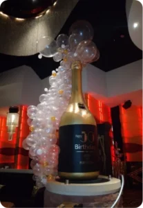 Giant birthday bottle with balloon arch.