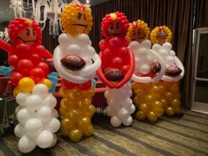 Balloon figures holding footballs in decorated room.