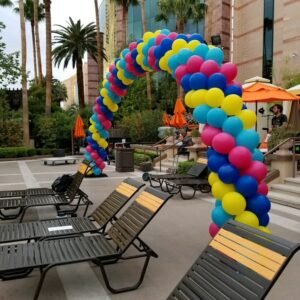 Colorful balloon arch over poolside chairs.